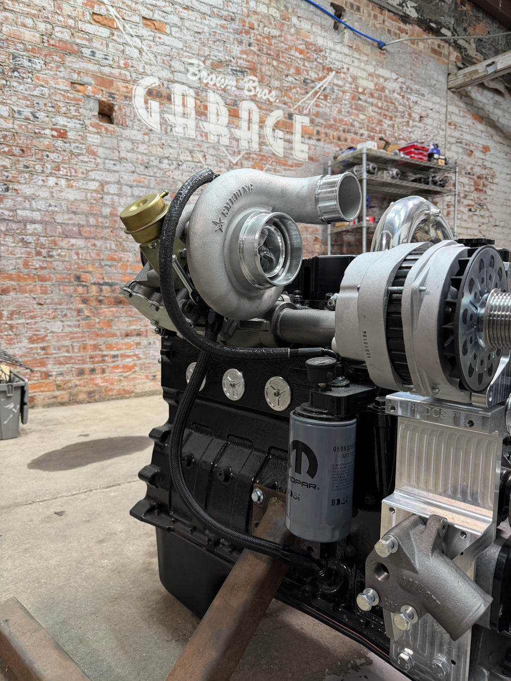 High-mount turbo on a Cummins with Brown Bros. oil feed and drain lines, in front of the Brown Bros. Garage brick wall