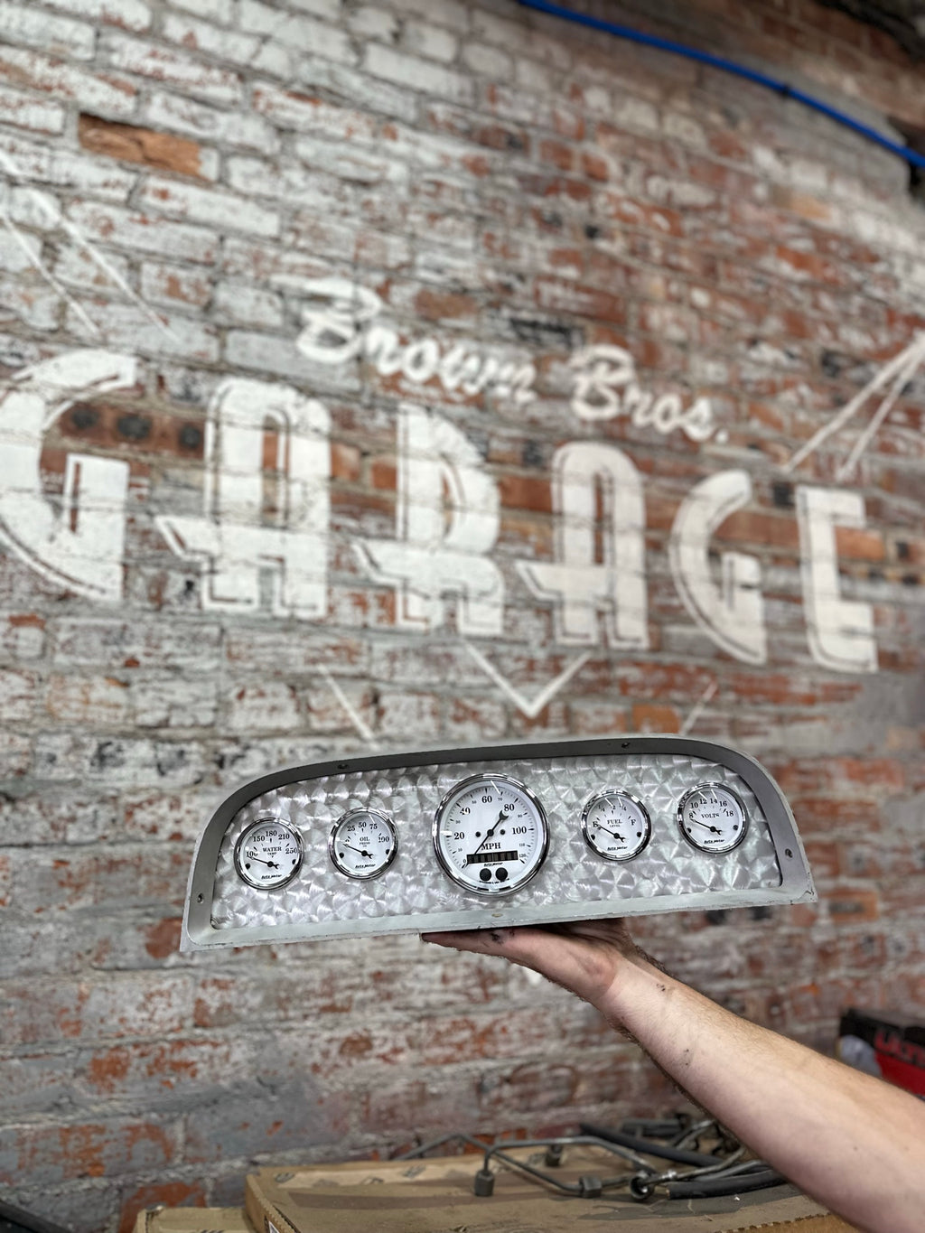 1960–1963 Chevy gauge cluster with AutoMeter gauges held up in front of the Brown Bros. Garage wall
